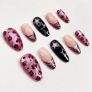 Puede incluir: Una colecci&oacute;n de u&ntilde;as postizas con varios dise&ntilde;os. Algunas u&ntilde;as presentan un estampado de leopardo rosa brillante, mientras que otras tienen una base negra con un dise&ntilde;o de estrella rosa. Varias u&ntilde;as tienen una base nude con rayas de cebra rosas.