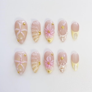 Pu&ograve; includere: Un set di dieci unghie finte con vari design. Le unghie sono principalmente rosa chiaro con accenti bianchi, gialli e dorati. Alcune unghie presentano disegni floreali e a conchiglia in 3D, mentre altre hanno un aspetto semplice ed elegante.