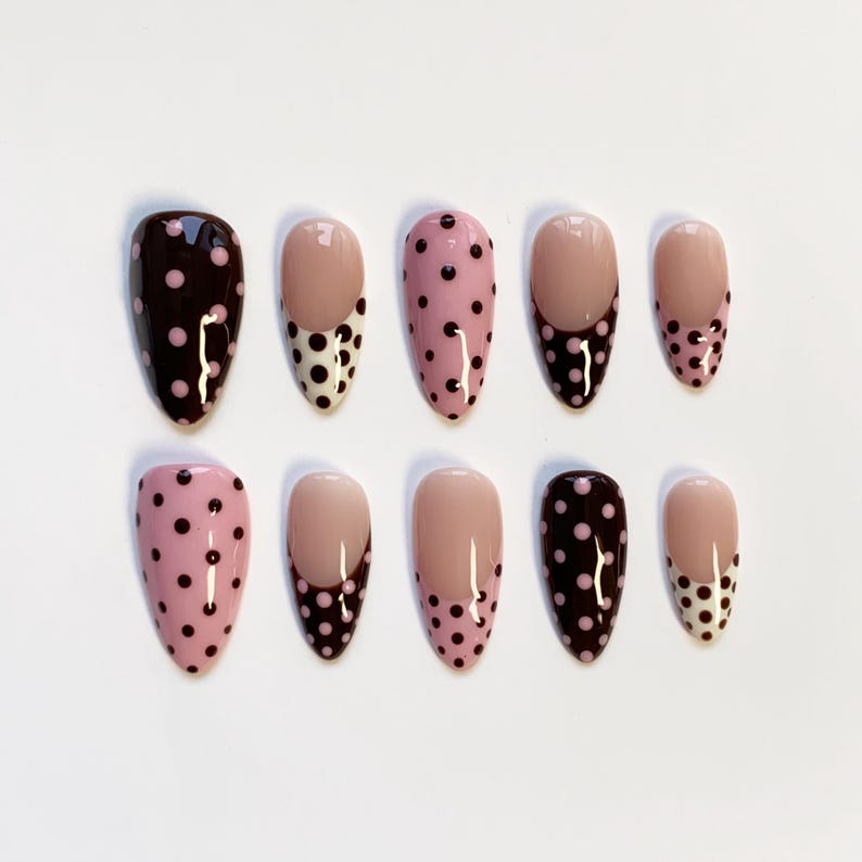Peut inclure: Dix faux ongles en forme d'amande. Les ongles pr&eacute;sentent divers motifs, notamment des couleurs unies, du rose &agrave; pois noirs et un motif &agrave; bout fran&ccedil;ais &agrave; pois noirs et blancs.