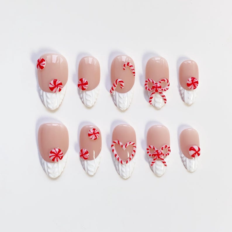 May include: A set of ten artificial nails with a light pink base, decorated with red and white candy cane and bow designs. The lower portion of each nail features a white, textured knit pattern, creating a festive holiday theme.