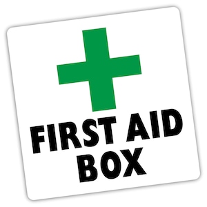 May include: A white square sticker featuring a green cross and the words "FIRST AID BOX" in bold black text. The sticker has a subtle shadow, giving a raised appearance.