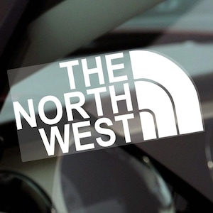 May include: White vinyl sticker featuring the text "THE NORTH WEST" in a bold, sans-serif font. The design incorporates a curved shape on the right. Suitable for application on vehicles or other surfaces.