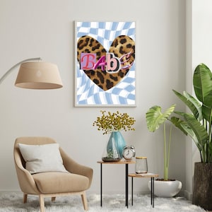 Può includere: Una stampa artistica incorniciata con un cuore leopardato e la parola "BABE" in uno stile di carattere misto. Lo sfondo presenta un motivo a scacchi blu e bianco. L'opera d'arte è esposta in una stanza con una sedia beige, una lampada da terra e piante.