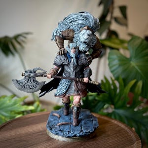 Puede incluir: Figura detallada de un guerrero sosteniendo un hacha grande, con una figura de león posada sobre sus hombros. El guerrero lleva armadura y botas, de pie sobre una base de piedra. El león tiene una melena de pelo fluido.