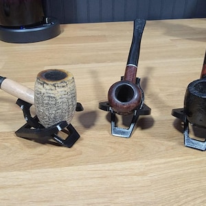 May include: Three wooden pipes on black metal stands. The pipes are different colors and styles. The stands are all the same design.