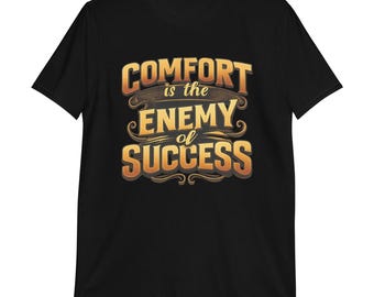 Puede incluir: Camiseta negra con la frase "COMFORT is the ENEMY of SUCCESS" en dorado y marrón. El texto tiene un diseño vintage y desgastado, centrado en la camiseta.