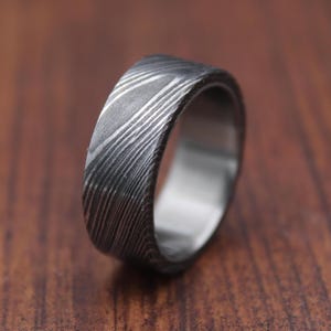 May include: A silver ring with a textured, patterned surface. The ring is made of metal and has a wide band.