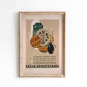 May include: Framed vintage print featuring a collection of Pennsylvania Dutch pottery and a black jug. The artwork includes the text "COLONIAL PENNSYLVANIA EXISTS TO-DAY IN MANY CHURCHES COSTUMES CRAFTS OF THE GERMAN SECTARIANS RURAL PENNSYLVANIA."