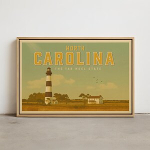 May include: A framed print with a vintage illustration of North Carolina. It depicts a black and white striped lighthouse, a white house, and the text "NORTH CAROLINA" and "THE TAR HEEL STATE" in gold lettering against a green and yellow backdrop.