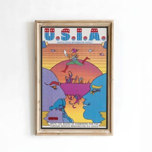 May include: A framed vintage poster with a colorful illustration. The top reads "U.S.I.A." with the text "UNITED STATES INFORMATION AGENCY". A figure runs across a sunset background. The bottom text reads "WRITE THE BOARD OF EXAMINERS FOR THE FOREIGN SERVICE, WASHINGTON, D.C. 20520."
