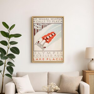May include: Framed vintage poster featuring a bobsled run scene. The artwork depicts a red bobsled with four figures racing down a snowy track, with text that reads "UP WHERE WINTER CALLS TO PLAY" and "OLYMPIC BOBSLED RUN LAKE PLACID."
