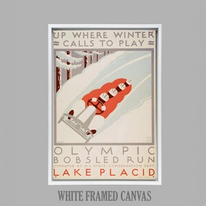 May include: White framed canvas print of a vintage Olympic bobsledding poster. The poster features a red bobsled racing down a snowy track, with the text "UP WHERE WINTER CALLS TO PLAY" at the top. The text "OLYMPIC BOBSLED RUN LAKE PLACID" is also visible.