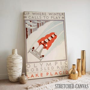 May include: A vintage-style stretched canvas print featuring a bobsled run scene. The artwork showcases a red bobsled with a driver and passengers racing down a snowy track, with text that reads "UP WHERE WINTER CALLS TO PLAY" and "OLYMPIC BOBSLED RUN LAKE PLACID".