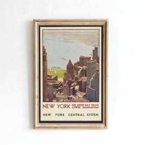 May include: A framed vintage travel poster of New York City, featuring a detailed illustration of the city skyline and harbor. The poster has a gold-colored frame and includes the text "NEW YORK" and "NEW YORK CENTRAL SYSTEM". The artwork is in shades of brown, beige, and blue.