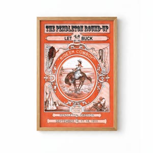 May include: A framed vintage poster for the Pendleton Round-Up rodeo. The orange and brown artwork features a cowboy riding a bucking bronco, with text that reads "Ride 'Em Cowboy" and "Let 'Er Buck". The poster is dated September 16, 17, 18, 1910.