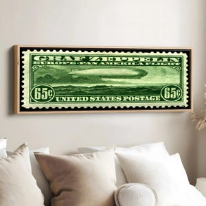 May include: A framed print of a vintage United States postage stamp. The green stamp features the text "GRAF ZEPPELIN EUROPE-PAN AMERICA FLIGHT" and a depiction of an airship. The stamp is valued at 65 cents.