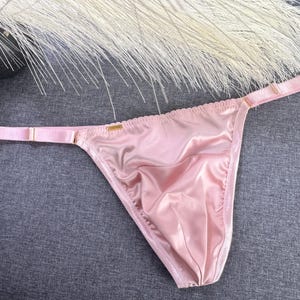 May include: A pink satin thong with adjustable straps. The thong is made of a soft, silky material and has a low-rise cut.