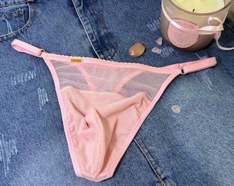 Op de afbeelding: Roze doorschijnende lingerie met een delicate kantversiering en gouden hardware. De lingerie heeft een lage taille en een stringrug.