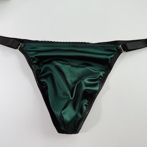 May include: A dark green satin thong with black trim and adjustable straps. The thong features a smooth, shiny fabric and a classic design. The straps are black with gold-colored metal hardware.
