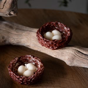 Spring inspired handmade bird nest candles with white eggs on wooden slab, minimalist Easter decoration.
