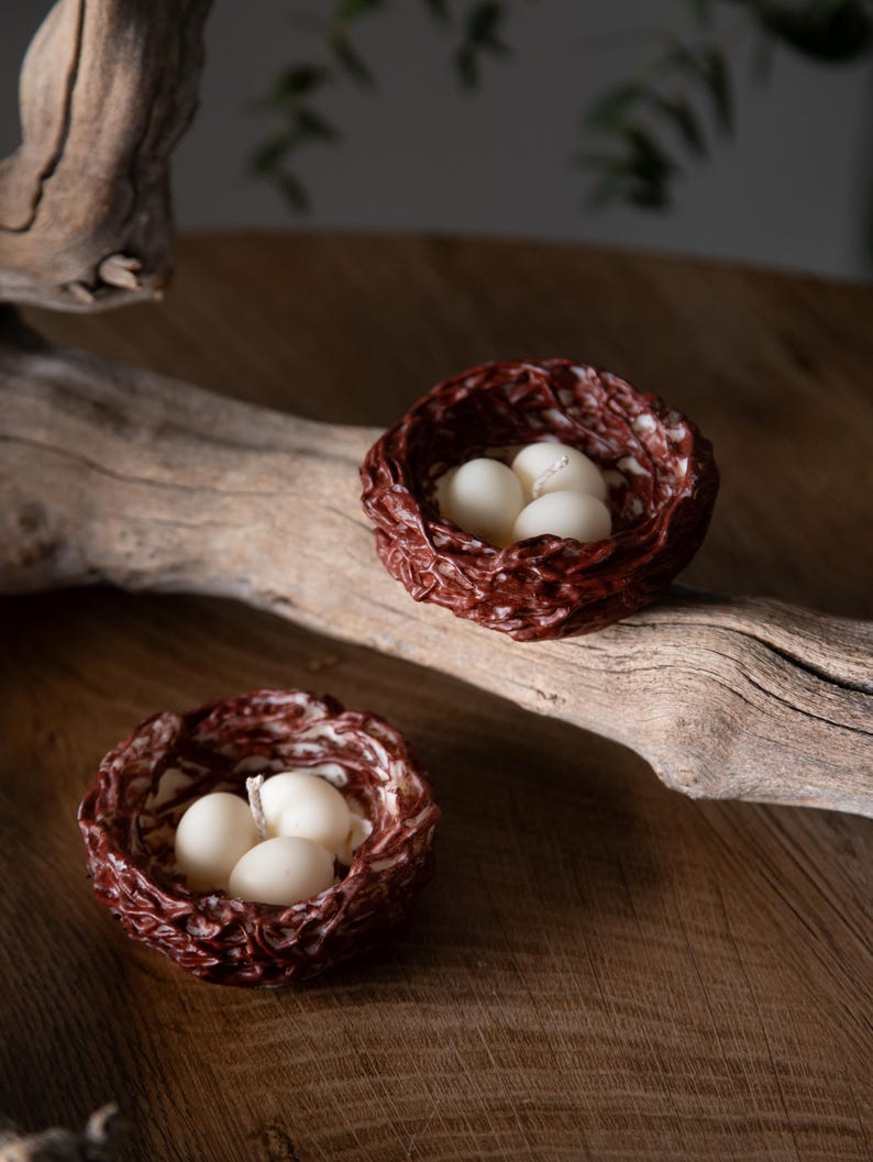 Spring inspired handmade bird nest candles with white eggs on wooden slab, minimalist Easter decoration.