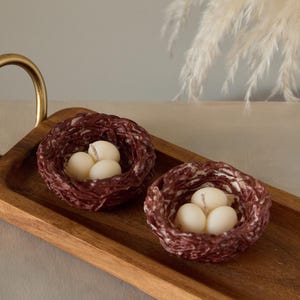 Set of small bird nest candles with white wax eggs displayed on wooden tray, nature inspired Easter home decor.