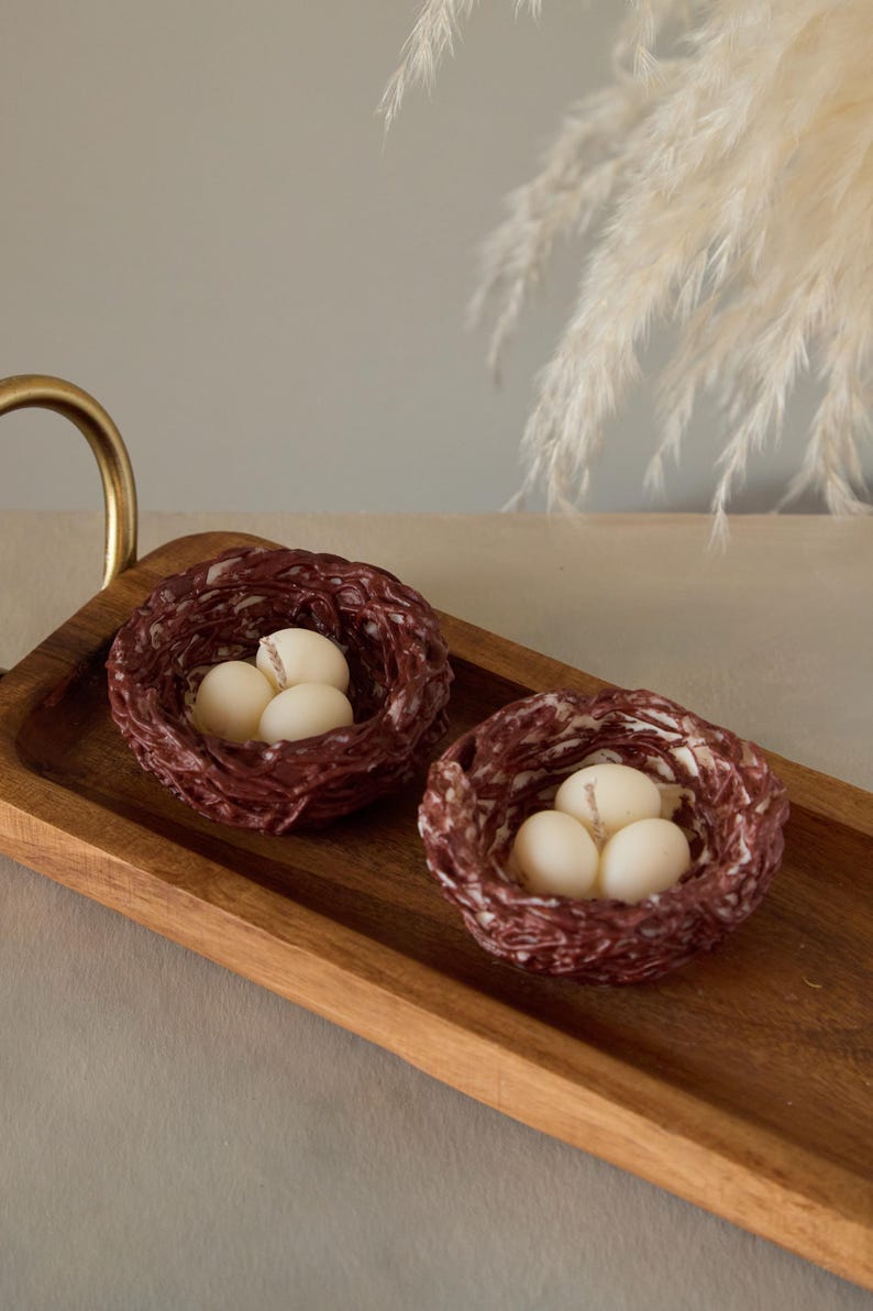 Set of small bird nest candles with white wax eggs displayed on wooden tray, nature inspired Easter home decor.