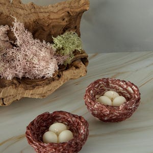 Decorative Easter nest candles with egg-shaped wax in woven twig nests, natural wood background, spring gift idea.
