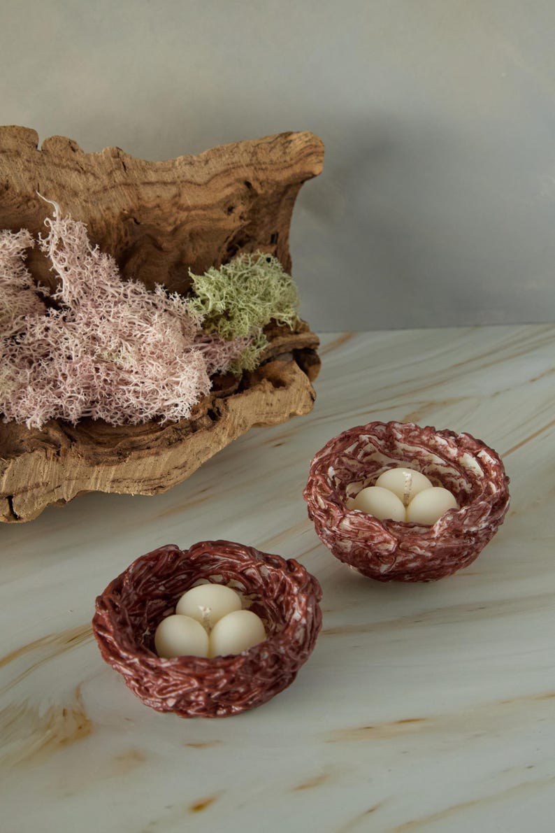 Decorative Easter nest candles with egg-shaped wax in woven twig nests, natural wood background, spring gift idea.