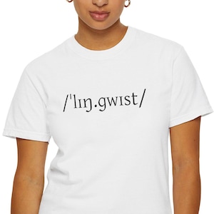 May include: A white t-shirt with the word "/lɪŋ.gwɪst/" printed in black. The shirt is a crew neck style and is being worn by a person wearing blue jeans.