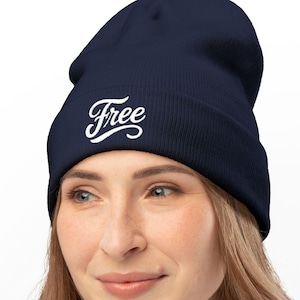 May include: A navy blue beanie hat with the word "Free" in white script. The hat is made of a soft material. The beanie is worn by a person.