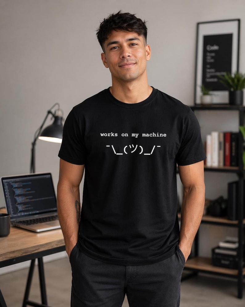 black t shirt with works on my machine text and shrug symbol worn by developer in modern workspace with laptop and coding screen