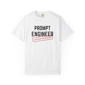 May include: A white short-sleeve t-shirt featuring the black text PROMPT ENGINEER centered on the chest. Below this, the words UNDER PROTEST are printed in red inside a rectangular outline that resembles a rubber stamp design.