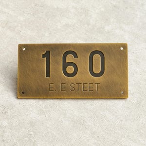 Puede incluir: Placa rectangular de número de casa de latón con el número "160" en negrita, en negro. El texto "E. E STREET" está debajo. La placa tiene una superficie texturizada y cuatro orificios de montaje.