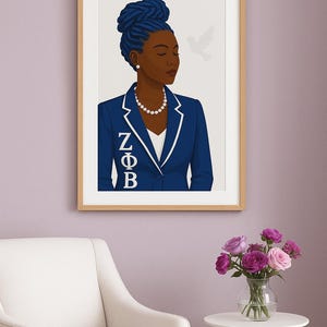 Puede incluir: Impresión artística enmarcada de una mujer con blazer azul con ribete blanco, con las letras griegas ZΦB. Tiene el pelo azul y un collar de perlas. Una paloma blanca está en el fondo. La impresión está en un marco de madera clara.