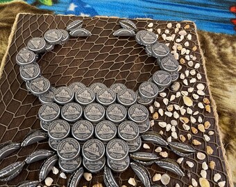 May include: A brown wooden square with a net pattern and a crab design made from Coors Light bottle caps and small seashells.