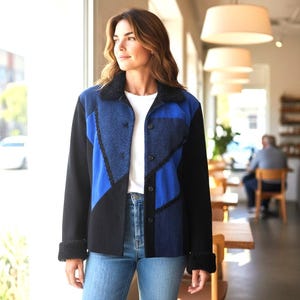 Puede incluir: Chaqueta patchwork azul, negra y azul marino con cuello y puños de piel sintética negra. La chaqueta tiene botones y se lleva con vaqueros azules y una camiseta blanca. El diseño presenta formas geométricas.