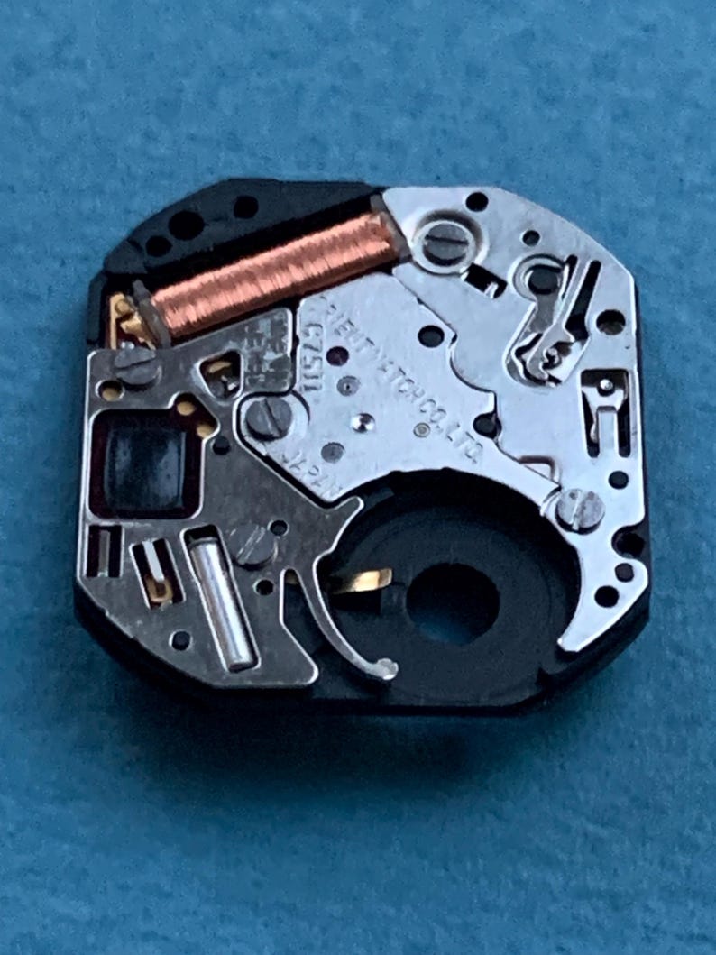 May include: Close-up of a watch movement with intricate gears, a copper coil, and the text "ORIENT WATCH CO. LTD." The watch mechanism is set against a blue background, showcasing its detailed internal components.