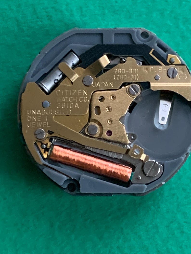 May include: Close-up of a Citizen watch movement. The watch mechanism features gold-colored gears, a copper coil, and a silver battery compartment. The text "CITIZEN WATCH CO. 3810A JAPAN" is visible.