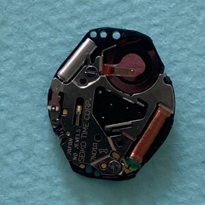 May include: A close-up of a watch movement with the text "JAPAN NO JEWELS SEIKO TIME CORP". The movement has a black base with silver and copper components. The watch movement is a 7N01A model.