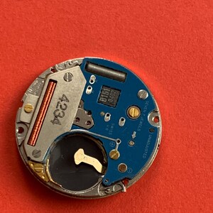 May include: A close-up of a watch movement with a blue circuit board and silver metal components. The number "4234" is printed on a silver component. The text "SEVEN 7 JEWELS" and "UNADJUSTED" are visible.