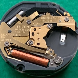 May include: Close-up of a Citizen watch movement, featuring gold-toned metal components, a copper coil, and the text "CITIZEN WATCH CO. 3810A JAPAN". The watch mechanism is set against a dark gray and black background.