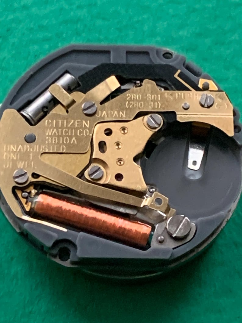 May include: Close-up of a Citizen watch movement, featuring gold-toned metal components, a copper coil, and the text "CITIZEN WATCH CO. 3810A JAPAN". The watch mechanism is set against a dark gray and black background.