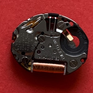 May include: Close-up of a watch movement with silver and gold components. The text "ORIENT WATCH CO., LTD. JAPAN D8040" is visible. The movement includes a copper coil and the text "ONE (1) JEWEL" and "UNADJUSTED".