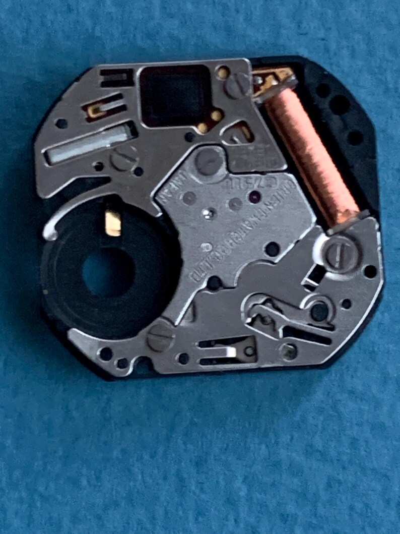 May include: Close-up of a watch movement with silver and gold components. The movement has a black, octagonal frame and a copper coil. The text "ORIENT WATCH CO LTD" and "JAPAN" are visible.