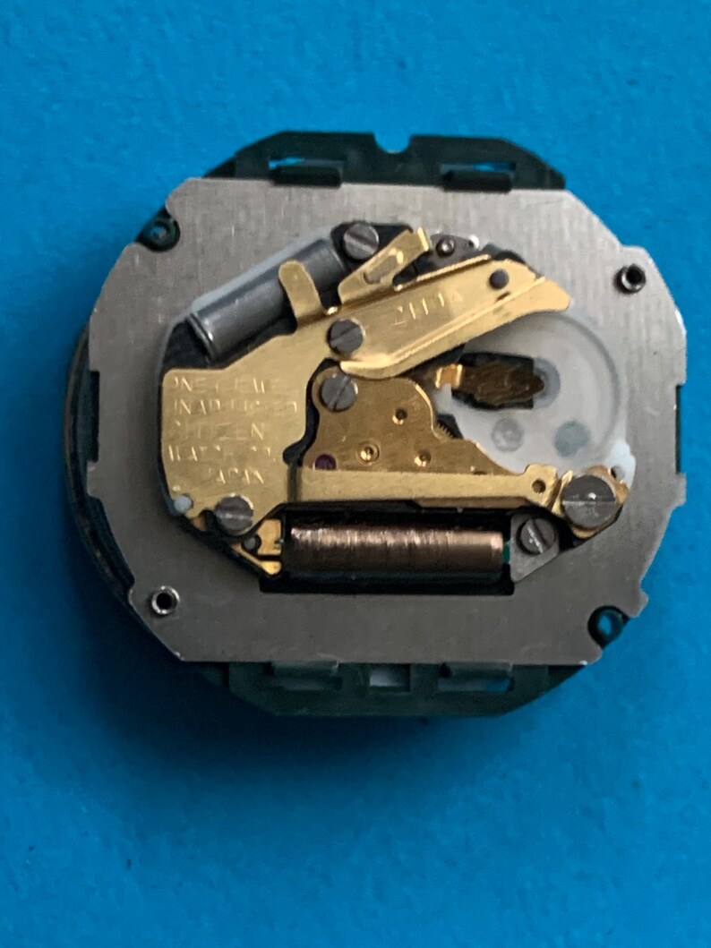 May include: A watch movement featuring gold-coloured gears and a silver-coloured base. The movement is inscribed with "ONE JEWEL UNADJUSTED CITIZEN JAPAN". This is a mechanical watch component.