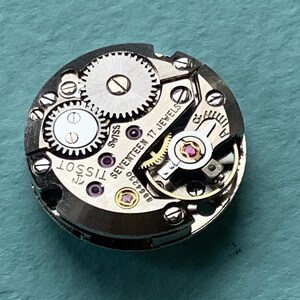 May include: Close-up of a silver Tissot watch movement with the text "Seventeen 17 Jewels" and "Swiss" printed on the face.
