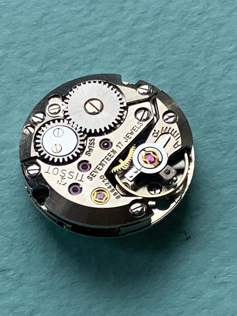 May include: Close-up of a silver Tissot watch movement with the text "Seventeen 17 Jewels" and "Swiss" printed on the face.