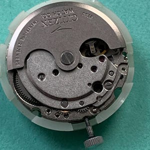 May include: A close-up of a Citizen watch movement, model 8200, with visible gears and components. The watch mechanism is silver-toned with the text "Citizen Watch Co." and "Twenty-one 21 Jewels" visible. The movement is encased in a clear plastic holder.