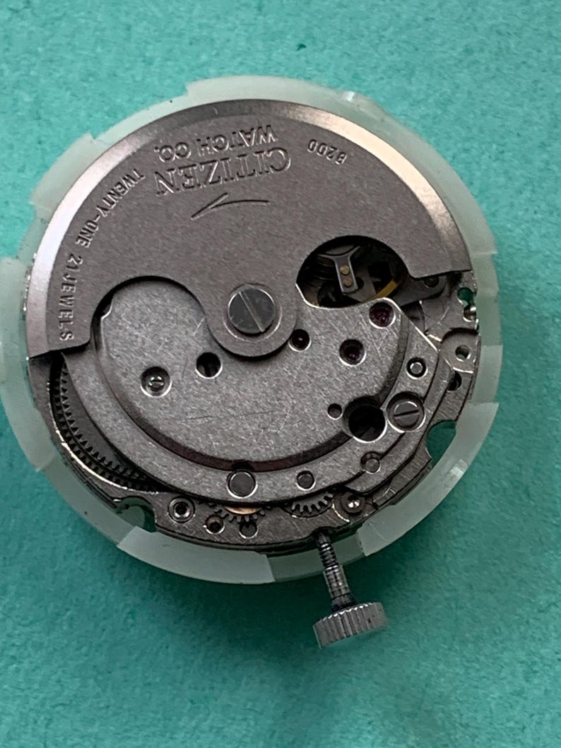 May include: A close-up of a Citizen watch movement, model 8200, with visible gears and components. The watch mechanism is silver-toned with the text "Citizen Watch Co." and "Twenty-one 21 Jewels" visible. The movement is encased in a clear plastic holder.